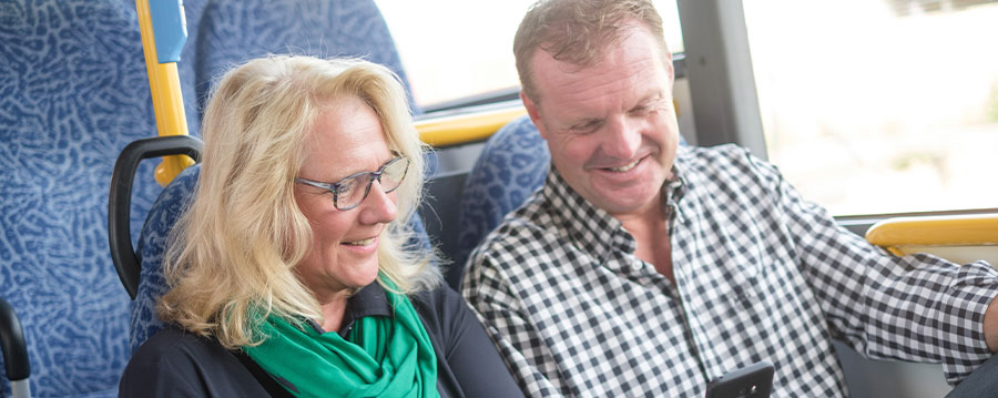 Man en vrouw op hun telefoon in de bus. 